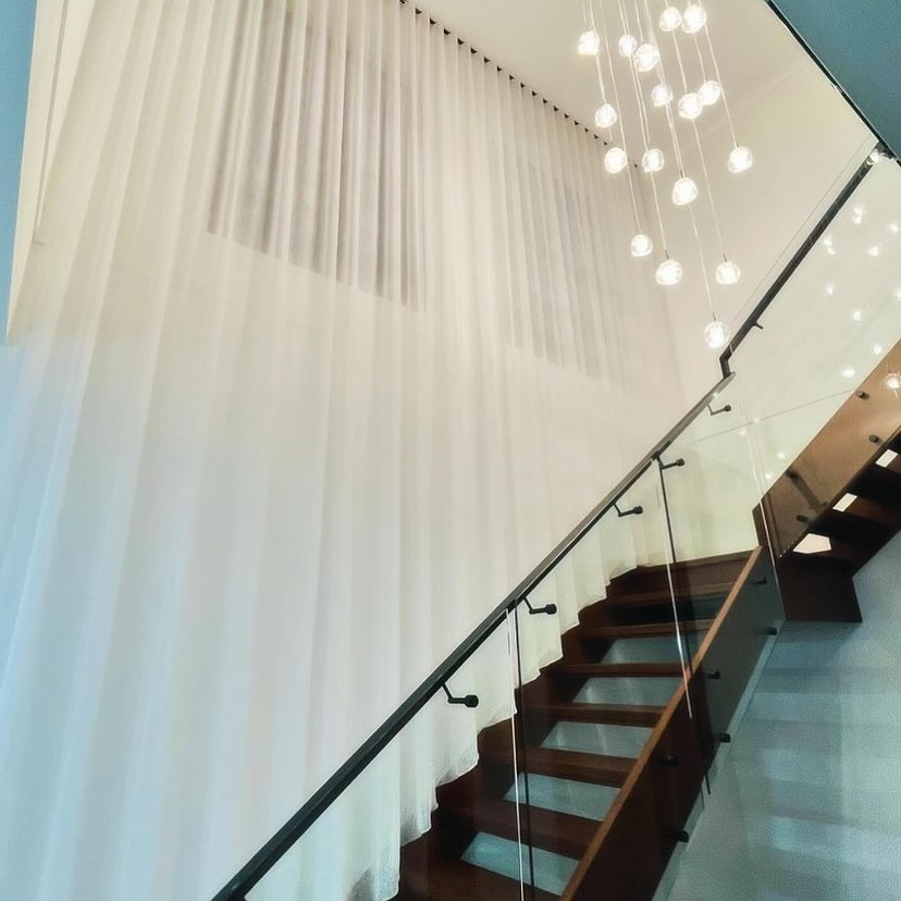 Sheer curtains installed above a staircase with pendant lighting